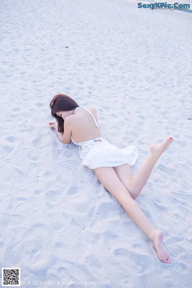 A woman in a white dress laying on the sand.
