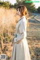 A woman in a trench coat standing in a field.
