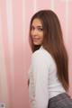 A woman with long brown hair standing in front of a pink wall.