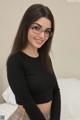 A woman wearing glasses sitting on a bed.