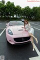 A woman leaning on the hood of a pink sports car.