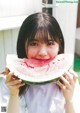 A young woman holding a slice of watermelon in front of her face.