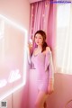 A woman standing in front of a pink wall with a neon sign.