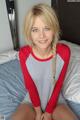 A woman sitting on top of a bed in a red and gray shirt.